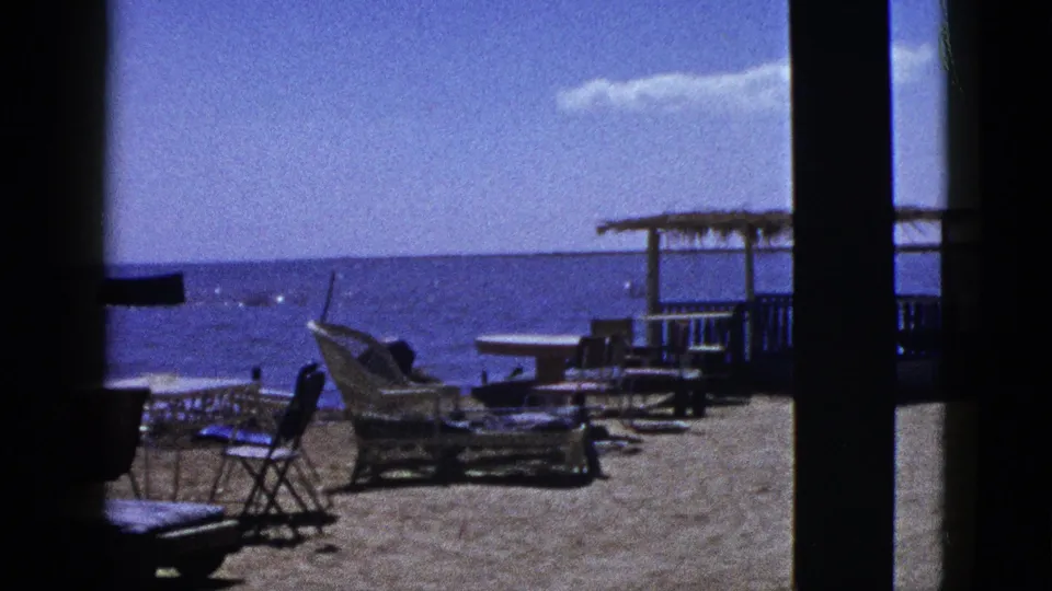 Palm Desert home-movie frame showing a poolside lounge setup, shaded vertical post, patio furniture, and a bright distant horizon.