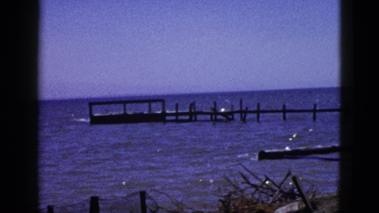 1953 8mm view of the Salton Sea shoreline with blue water, a low wooden dock, and dark film-gate borders.