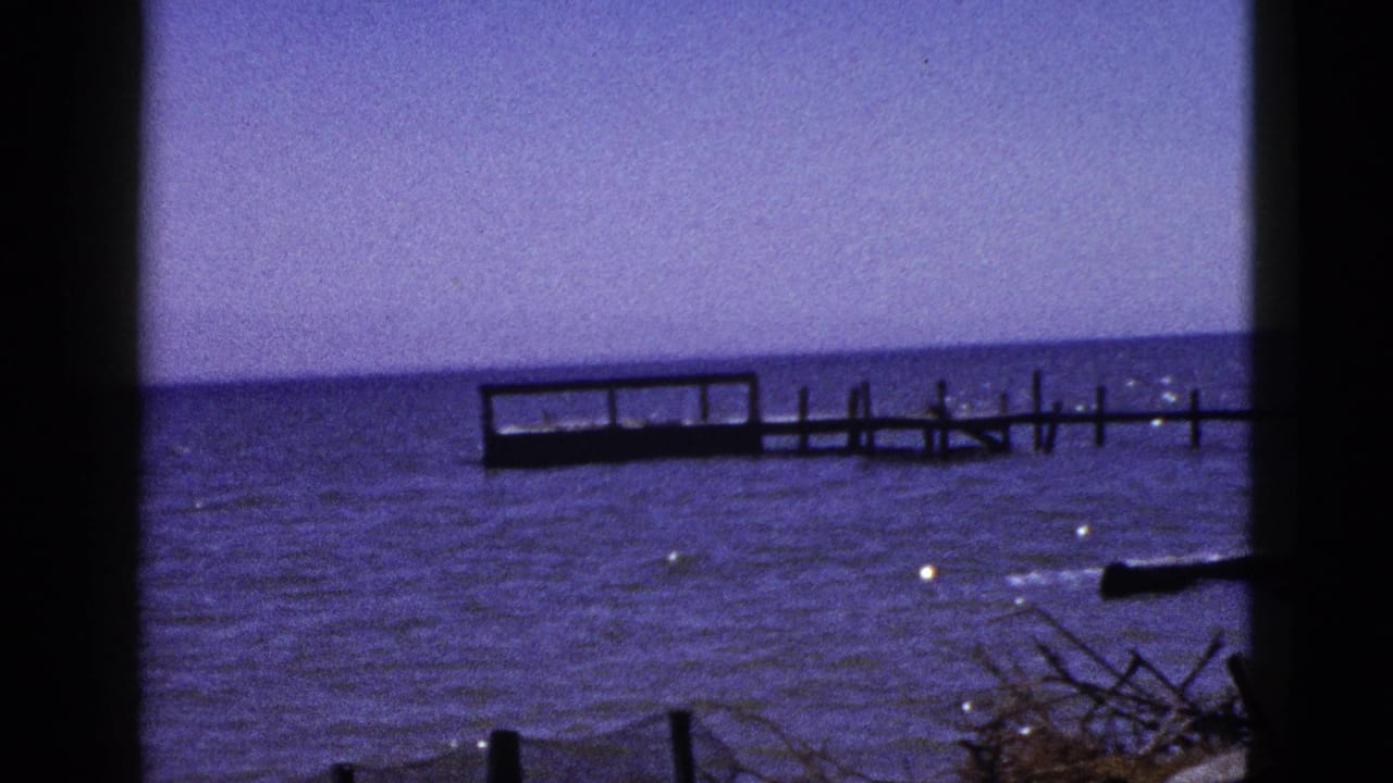 Wooden dock and rippling blue water framed by dark film edges.