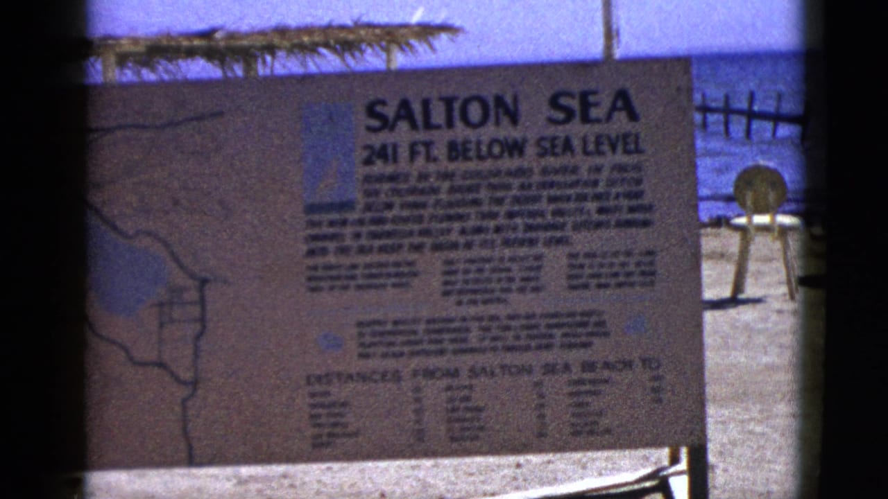 Salton Sea informational sign on sandy beach with blue water behind it.