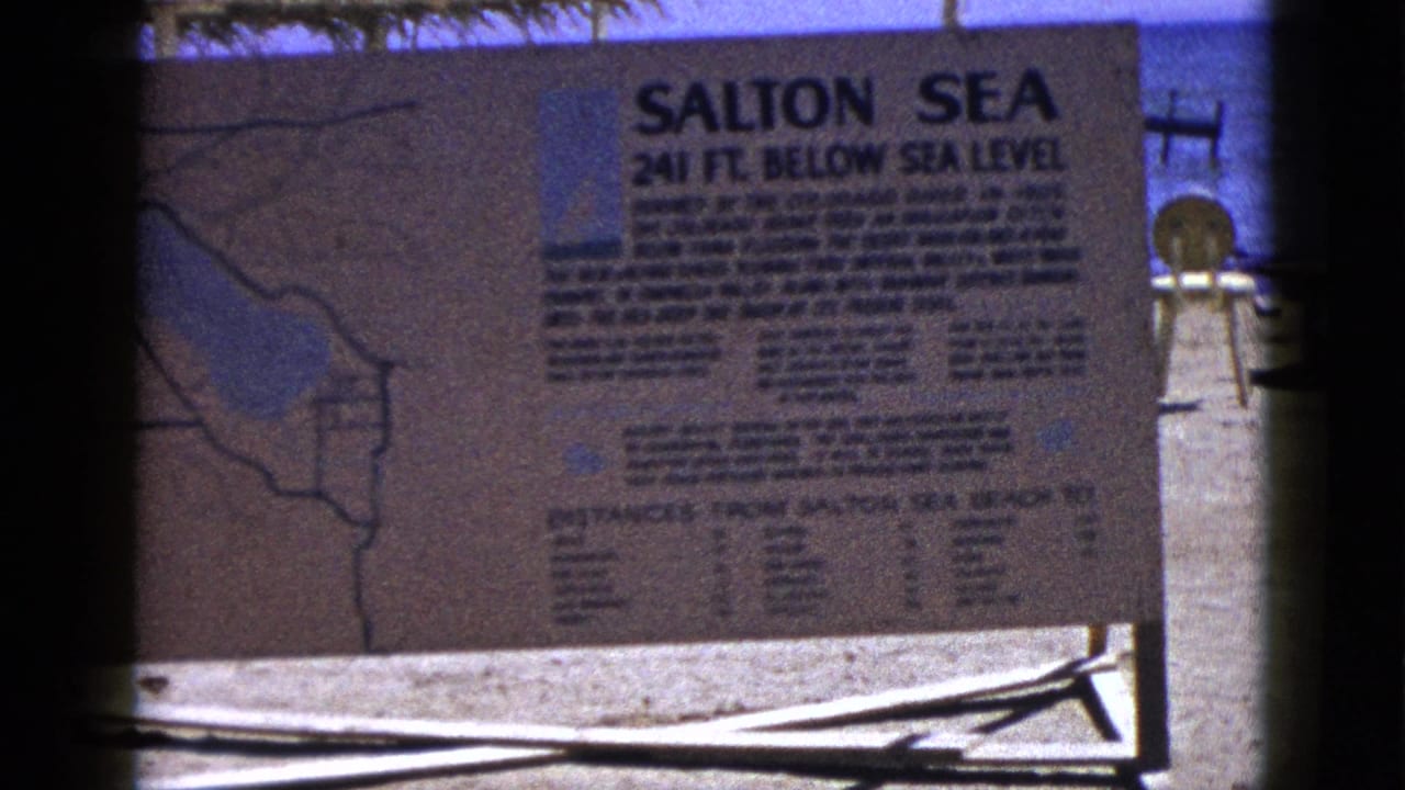 Salton Sea informational sign beside blue water and a sandy shore.