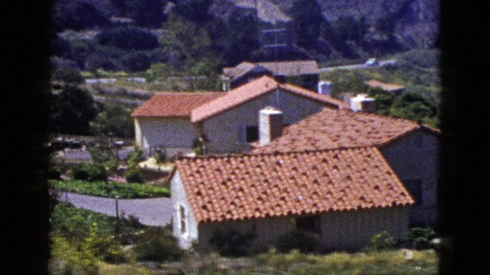 1953 8mm view of Palm Springs area residences with red tile roofs, garden plantings, and rugged hills beyond.