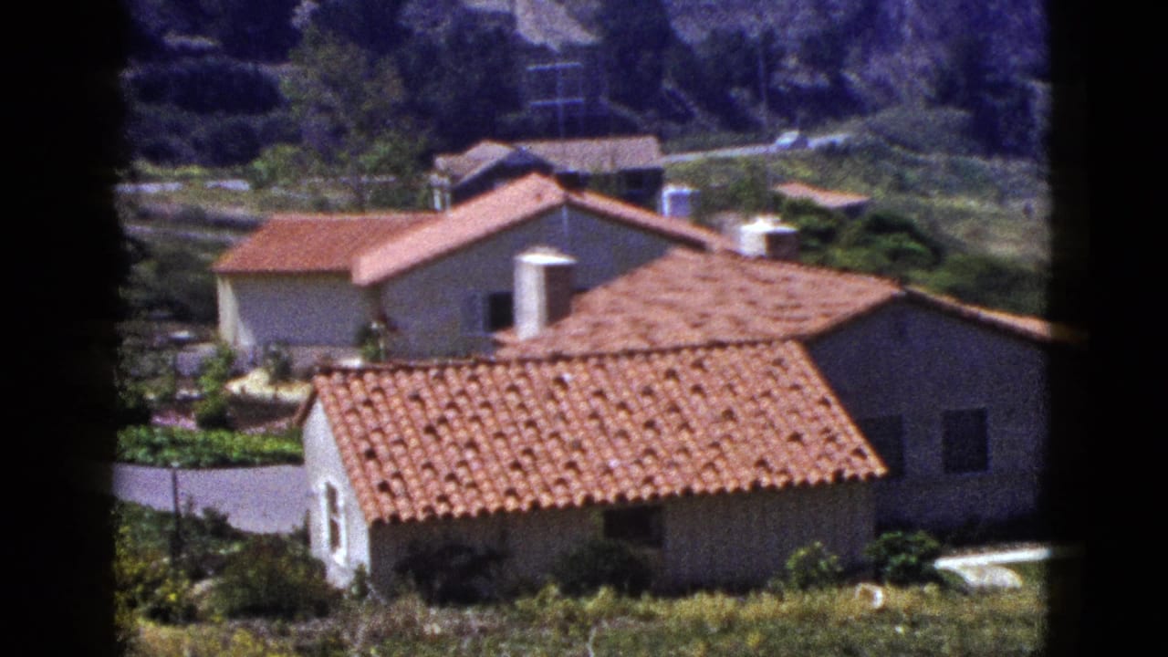 Stucco houses with red tile roofs on a hillside, seen through a contact-sheet frame edge.
