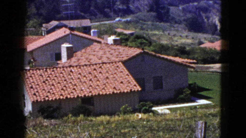Palm Springs hillside residences with terracotta roofs, stucco walls, lawns, and mountain terrain in the background.