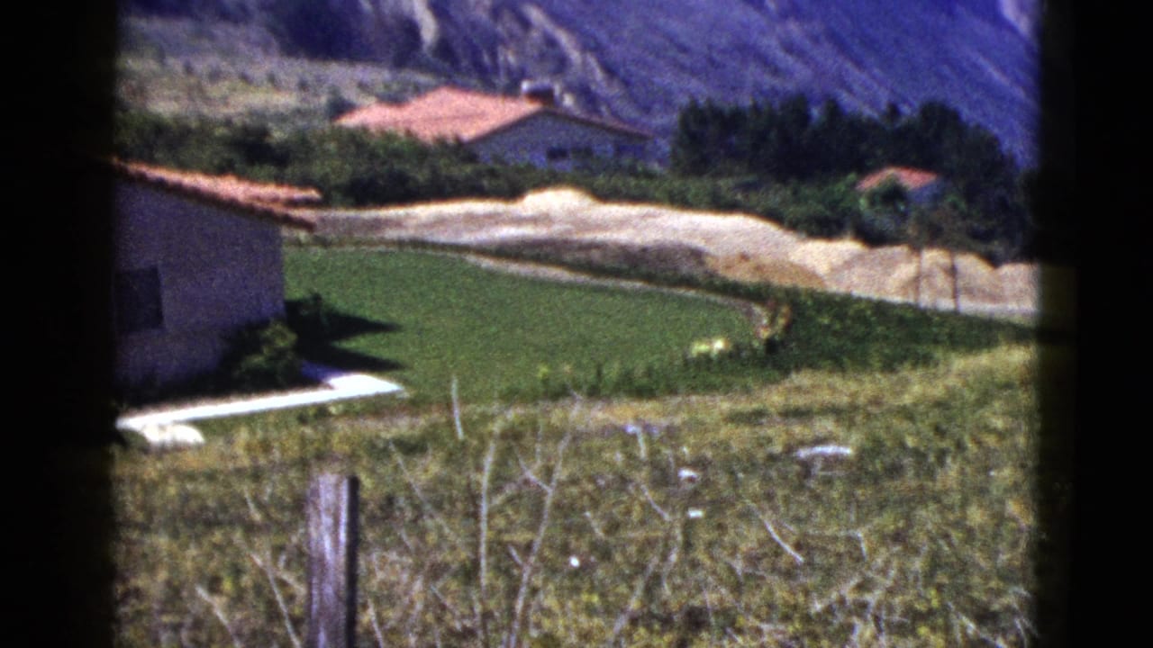 Hillside lawn and red-roofed houses below rocky slopes.