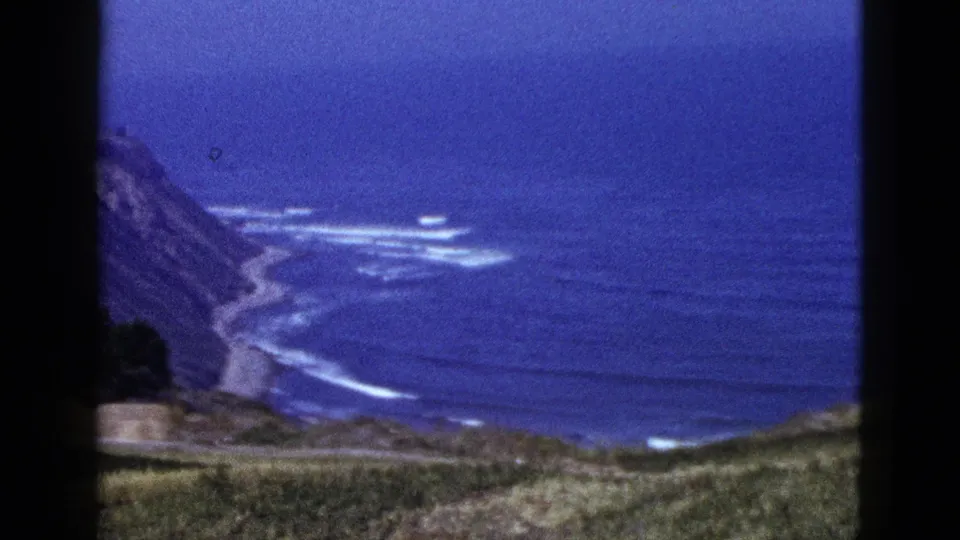 1953 8mm travel footage shows a steep California coastal cliff with surf bands below and soft blue film color.