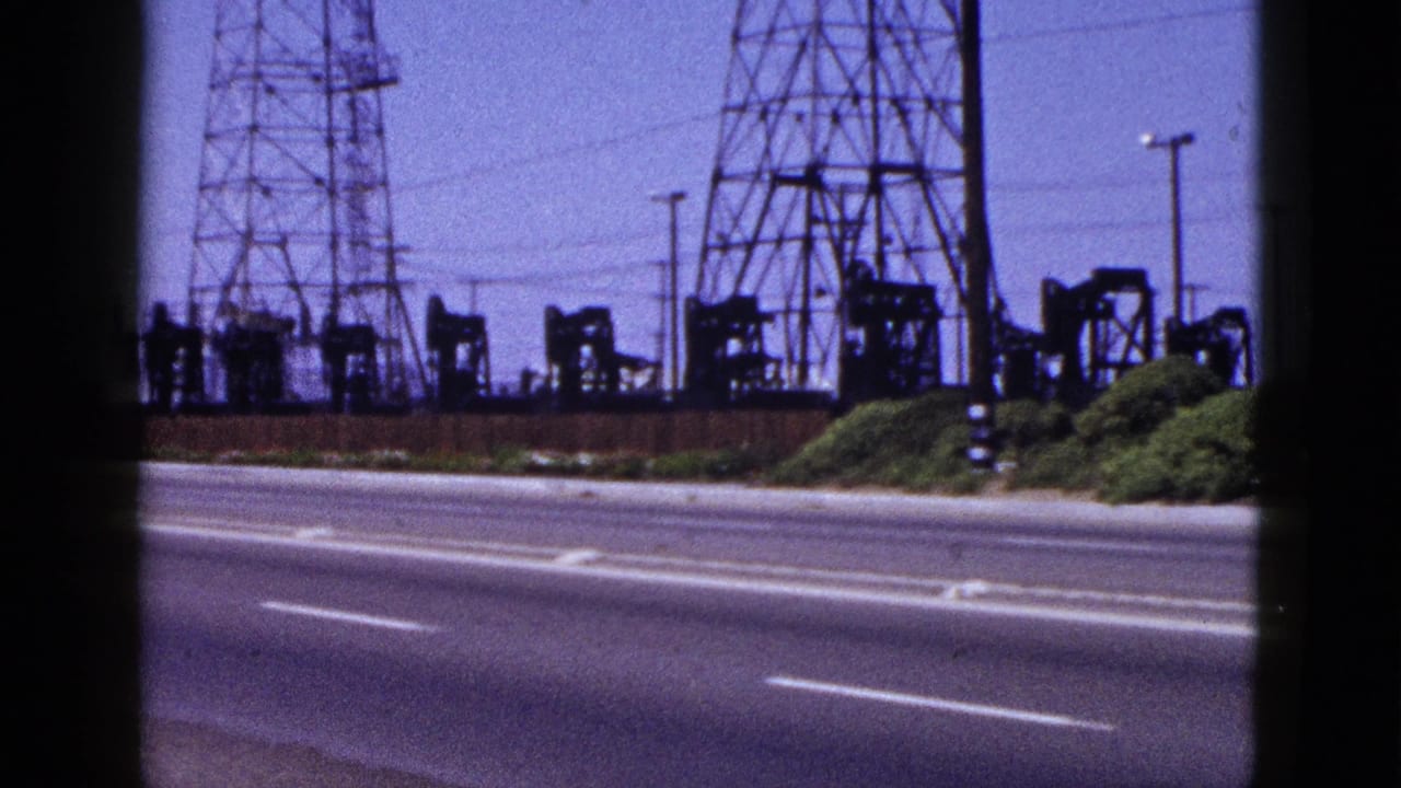 1953 Palm Springs roadside view with oil pumpjacks, lattice transmission towers, shrubs, and empty traffic lanes.
