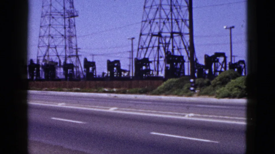 1953 Palm Springs roadside view with oil pumpjacks, lattice transmission towers, shrubs, and empty traffic lanes.