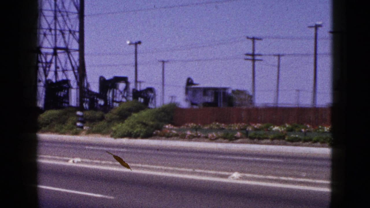1953 Palm Springs-area roadside view with oil pumpjacks, power lines, utility poles, low vegetation, and a paved road in the foreground.