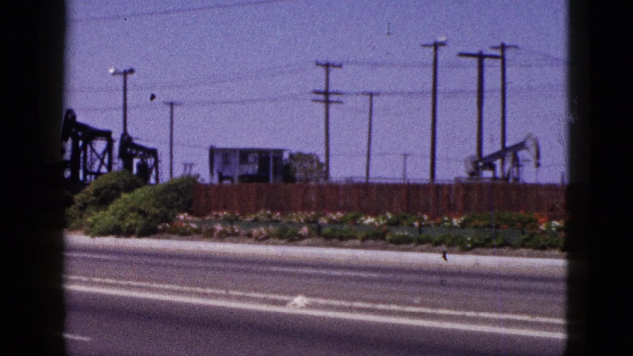 Palm Springs roadside oil-field scene with several pumpjacks, overhead utility lines, poles, fencing, and desert roadside planting.