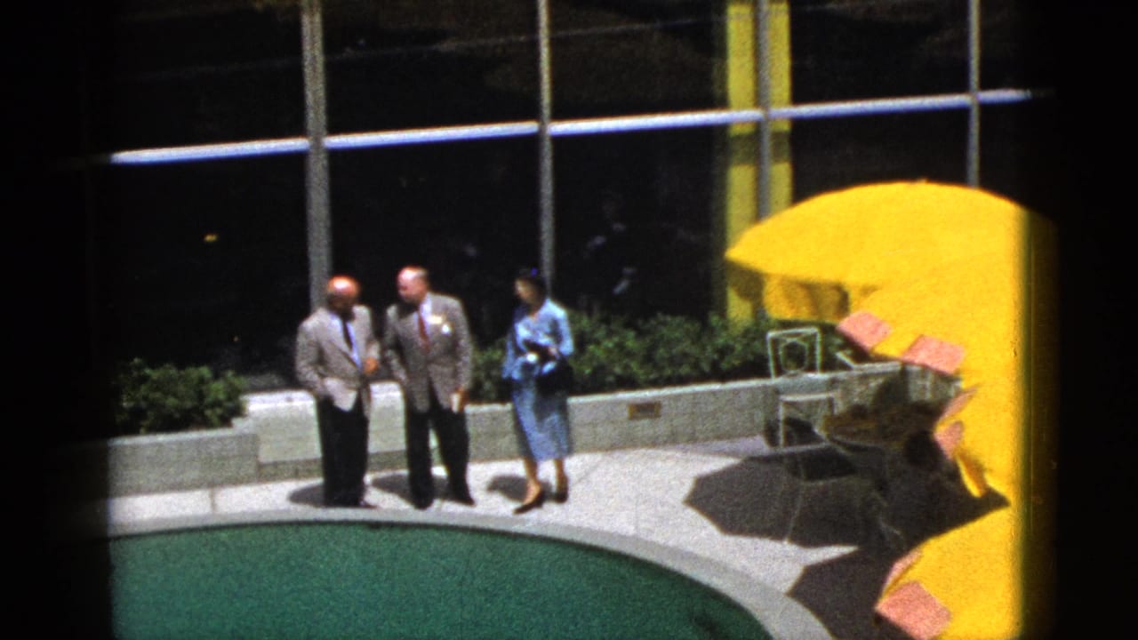 Three adults stand near a curved pool at a Palm Springs vacation setting, with bright yellow umbrellas and patio seating behind them.