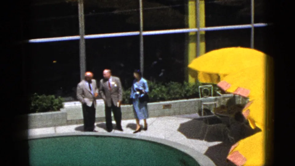 Three adults stand near a curved pool at a Palm Springs vacation setting, with bright yellow umbrellas and patio seating behind them.