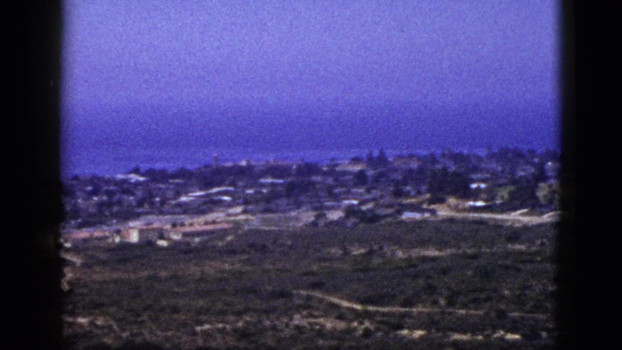 Coastal settlement and ocean horizon viewed through dark vertical film-frame edges.