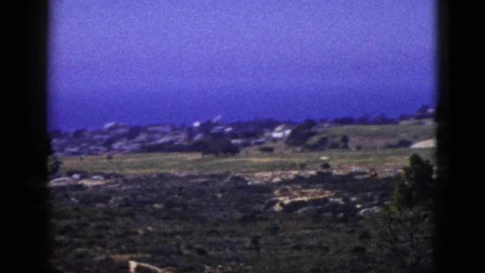 1953 California coastal landscape with open fields, low buildings, dirt tracks, and the Pacific Ocean visible beyond the hillside town.