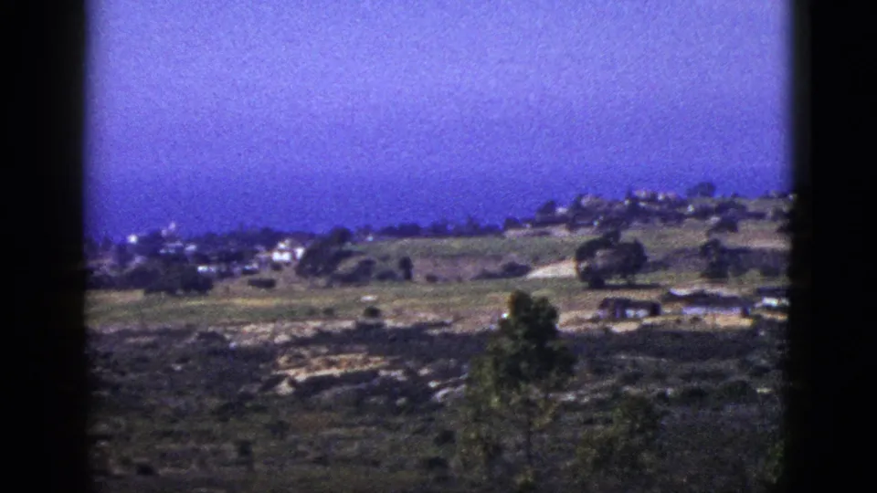 1953 California home-movie frame of low hills, distant houses, open ground, trees, and dark 8mm frame edges.