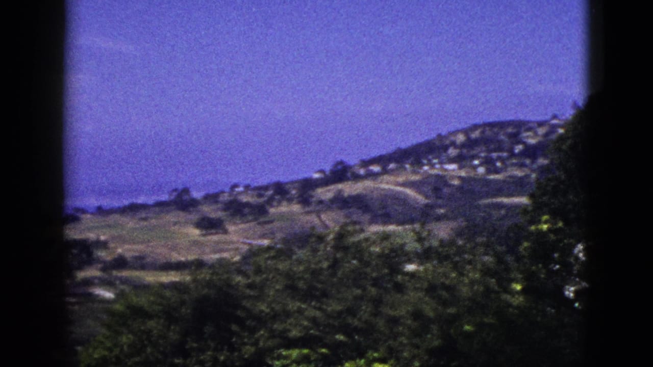 Hillside homes and coastal slopes seen through dark film-frame edges.