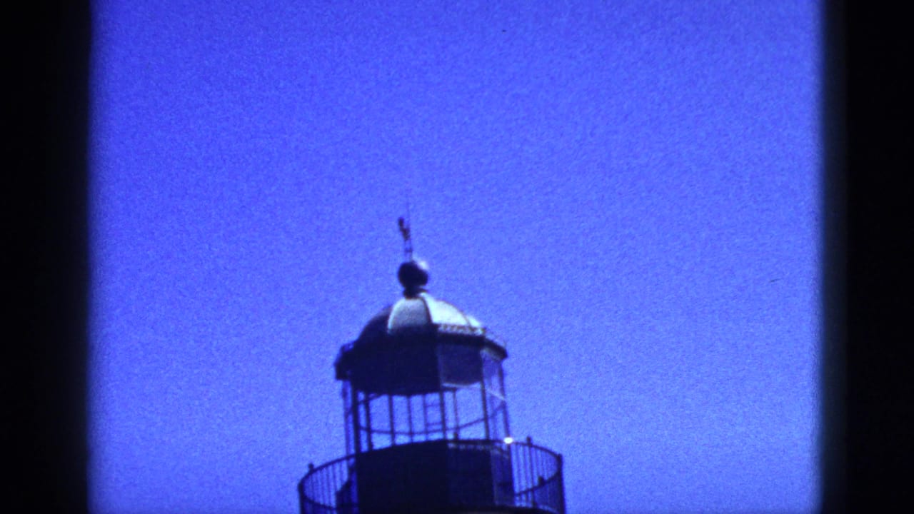 1953 California 8mm frame showing the upper lantern room and dome of a lighthouse-like structure against a vivid blue sky.