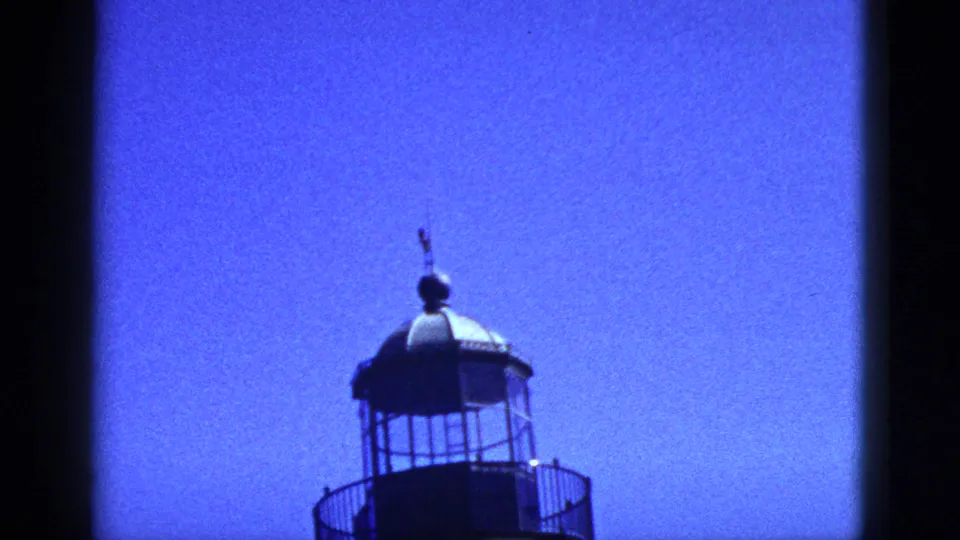 1953 California 8mm frame showing the upper lantern room and dome of a lighthouse-like structure against a vivid blue sky.