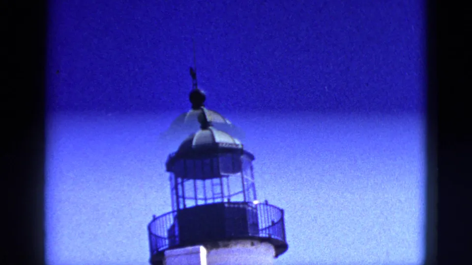California 1953 home-movie still with a lighthouse-like lantern room, black railings, and a white tower beneath a blue sky.