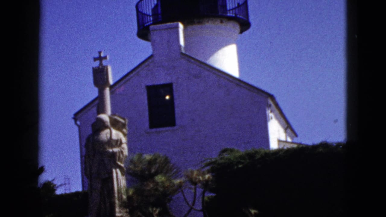 White lighthouse facade with black lantern room, lit window, robed statue, foliage, and dark film borders.