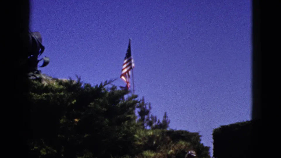 1953 California 8mm frame showing a U.S. flag over trees, with a dark edge and soft saturated color from the film scan.
