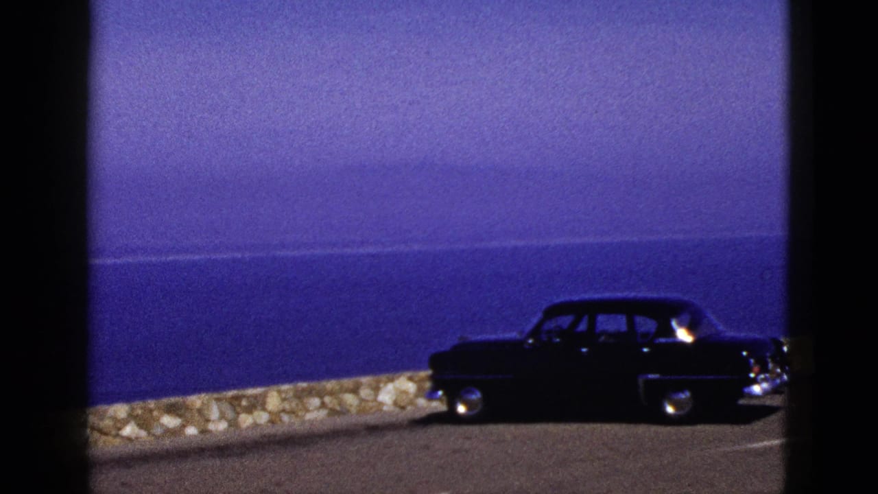 Dark sedan parked beside a stone wall overlooking blue ocean.