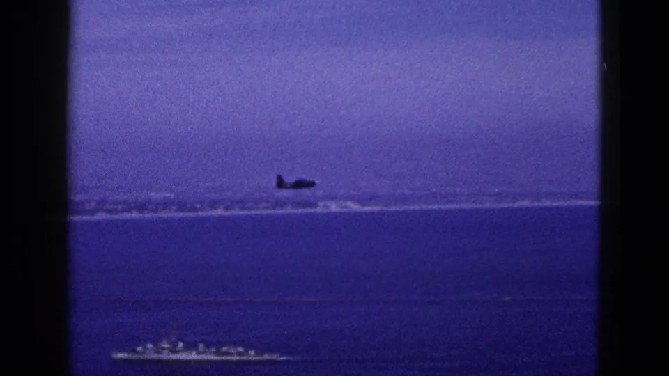 Small aircraft appears low over the water in a 1953 California coastal home-movie frame.