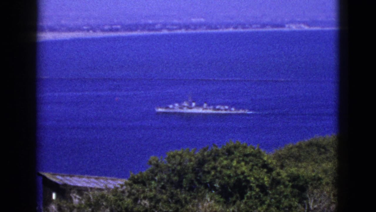 1953 California 8mm frame showing a distant ship crossing blue coastal water above dark green foreground trees.