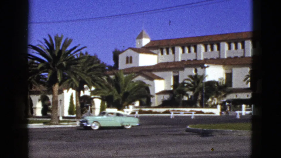 1953 California street scene with a mint-green car crossing before a white Spanish-style building and tall palms.