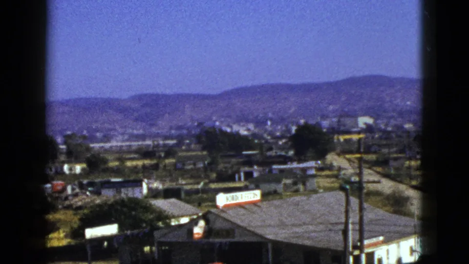 1953 California 8mm view over a small town with rooftops, signs, utility poles, roads, distant buildings, and mountain ranges.