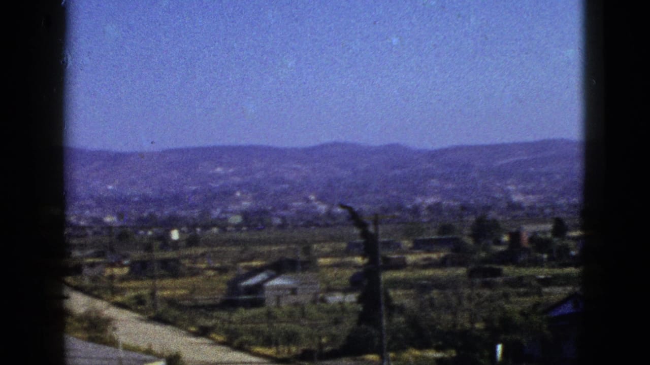 Rural valley landscape with hills, houses, and utility poles.