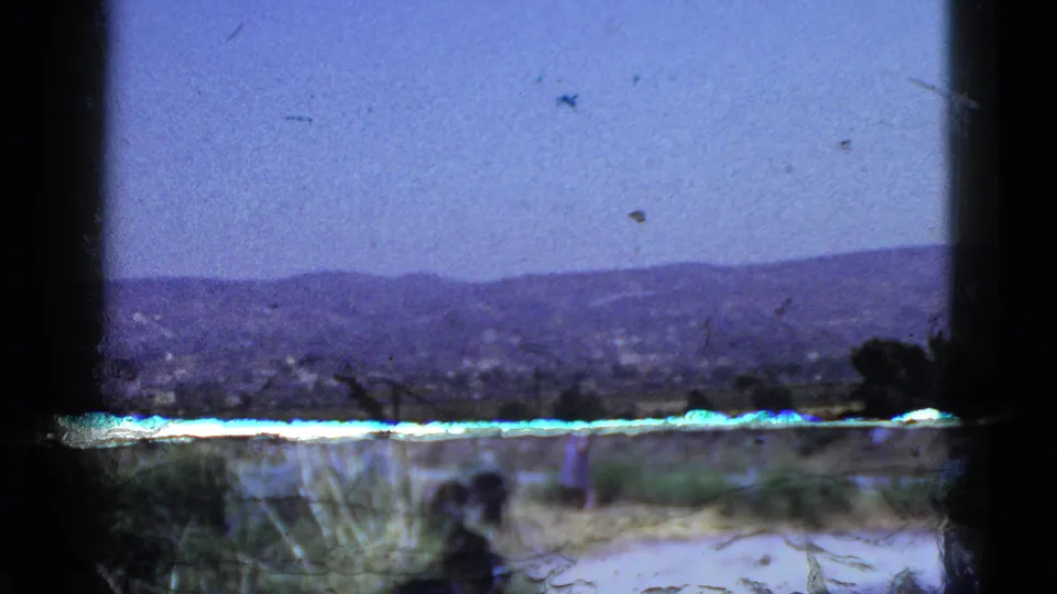 Soft 8mm frame of a California hillside and valley settlement, partly obscured by a bright ledge and dark window framing.