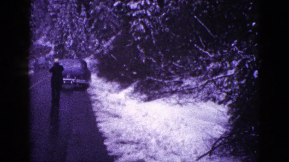Snowy California forest road in 1953 home-movie footage, with a person near a parked car during a winter roadside stop.