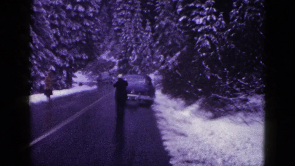 Closer 8mm view of a dark-clothed person and parked car along a snow-covered California forest road in 1953 footage.
