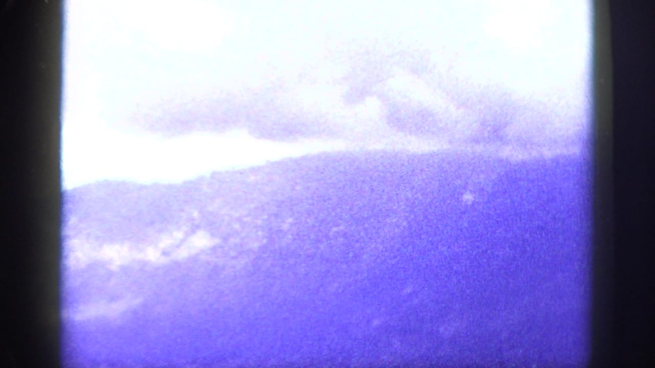 A heavily faded 8mm view of distant mountain ridges under cloud cover, with strong purple-blue color shift.