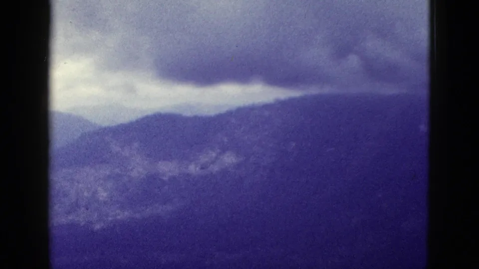 A distant California mountain view appears through faded 8mm color, showing ridges, low clouds, and soft handheld framing.