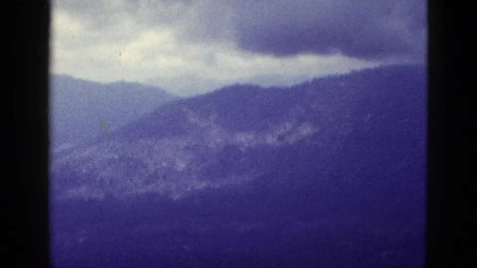 Layered mountain ridges fill the frame beneath a cloudy sky, rendered in soft, faded 1950s 8mm color.