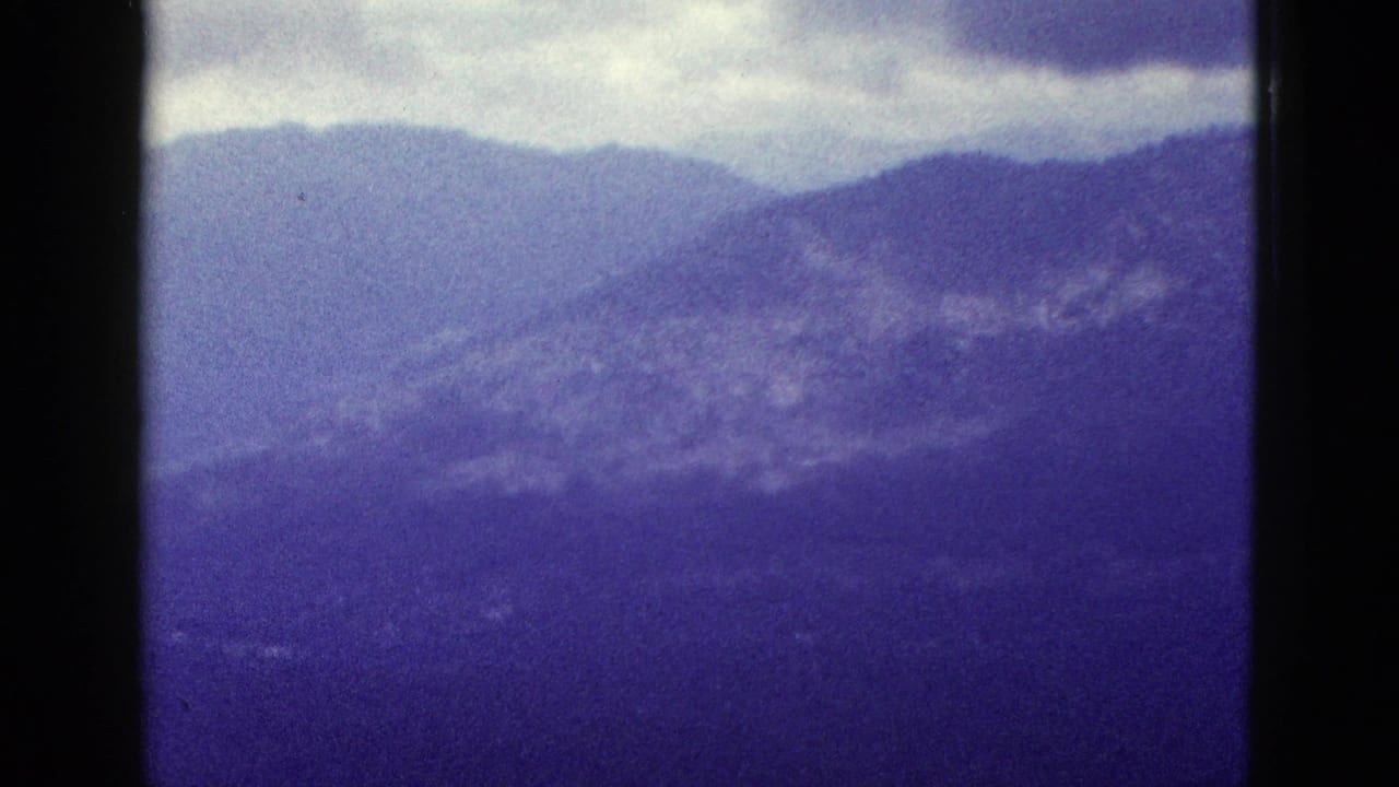 Aerial 8mm frame of California mountain ridges and cloud cover, with grain, softness, and purple color fading.