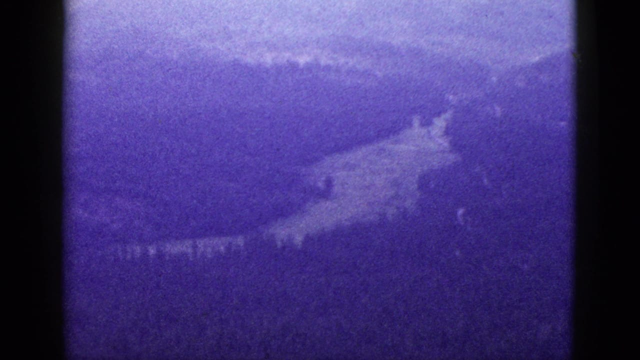 1953 California 8mm frame showing a hazy mountain valley and hillside under a purple-blue color shift.