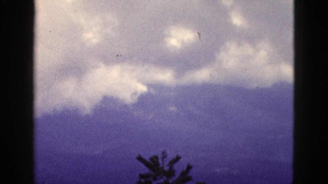 Cloudy sky over distant mountain ridges with a dark tree silhouette at the bottom.