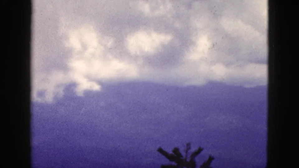 1953 California 8mm frame showing cloud layers above distant mountains and a low evergreen silhouette.