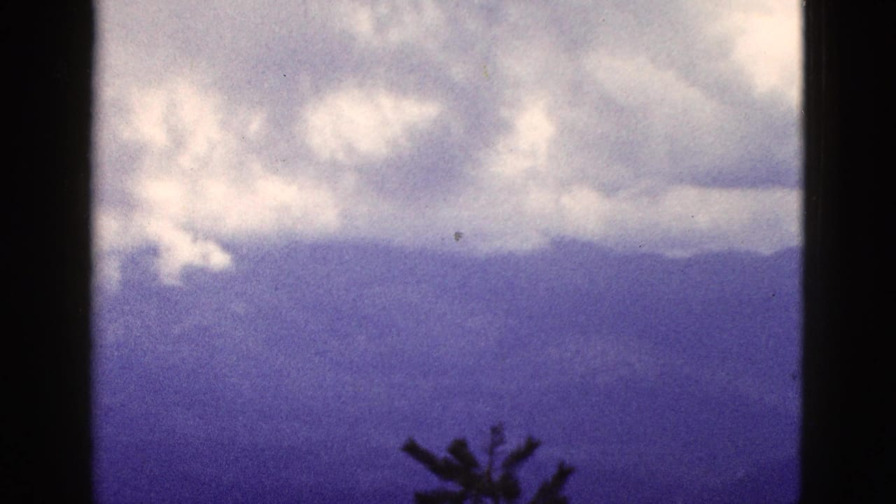 1953 California 8mm frame showing low clouds over distant mountain ridges with a blue-purple color shift and silhouetted treetop.