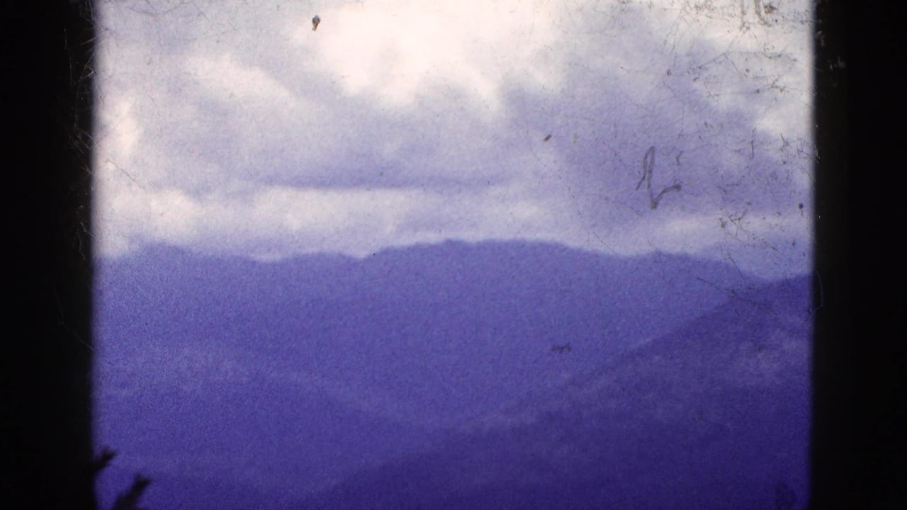 1953 California 8mm frame showing distant blue-purple mountain ridges under overcast clouds with heavy film borders.
