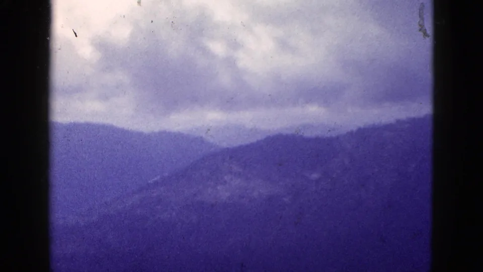 1953 California 8mm landscape view showing muted mountain layers below a heavy cloudy sky and aged film marks.