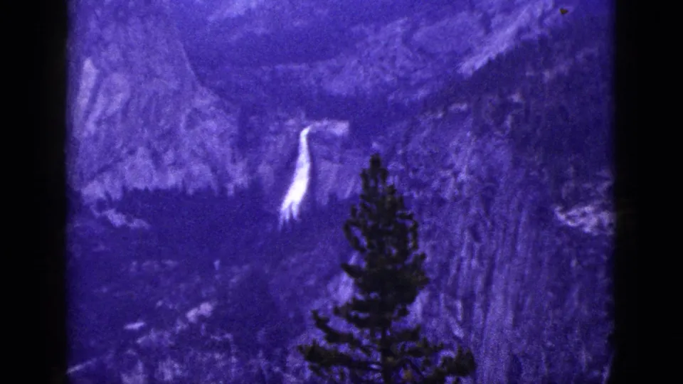 1953 California 8mm frame showing a white waterfall across a purple-toned mountain landscape with a pine silhouette in front.
