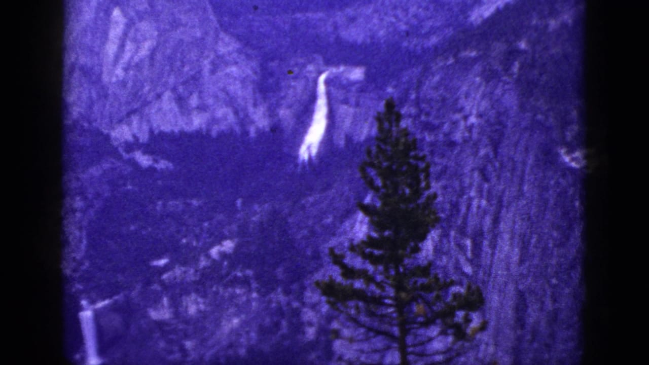 Waterfall and pine tree framed by dark film borders in a purple mountain landscape.