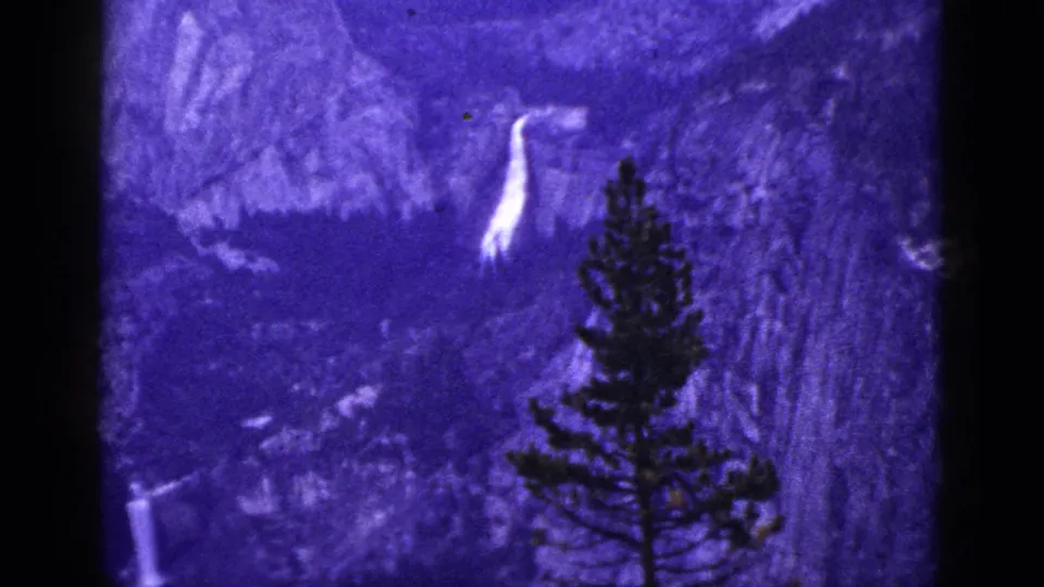 1953 California 8mm still with a bright waterfall high on the slope and a pine tree silhouetted at right.