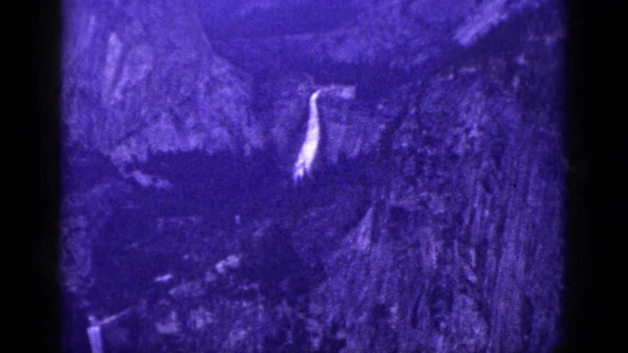 1953 California 8mm frame showing a small bright waterfall descending through a dark rocky mountain landscape.