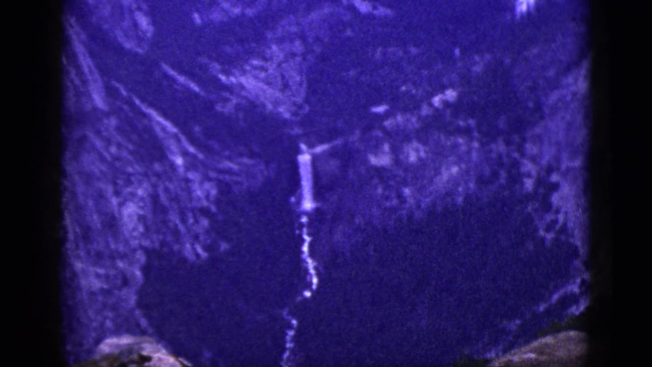 Distant waterfall and rugged mountain face in soft purple-blue film color.