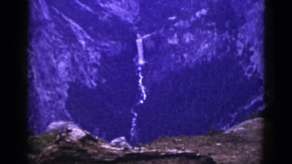 1953 California 8mm frame showing rocky foreground below a distant waterfall and dark mountain slope.